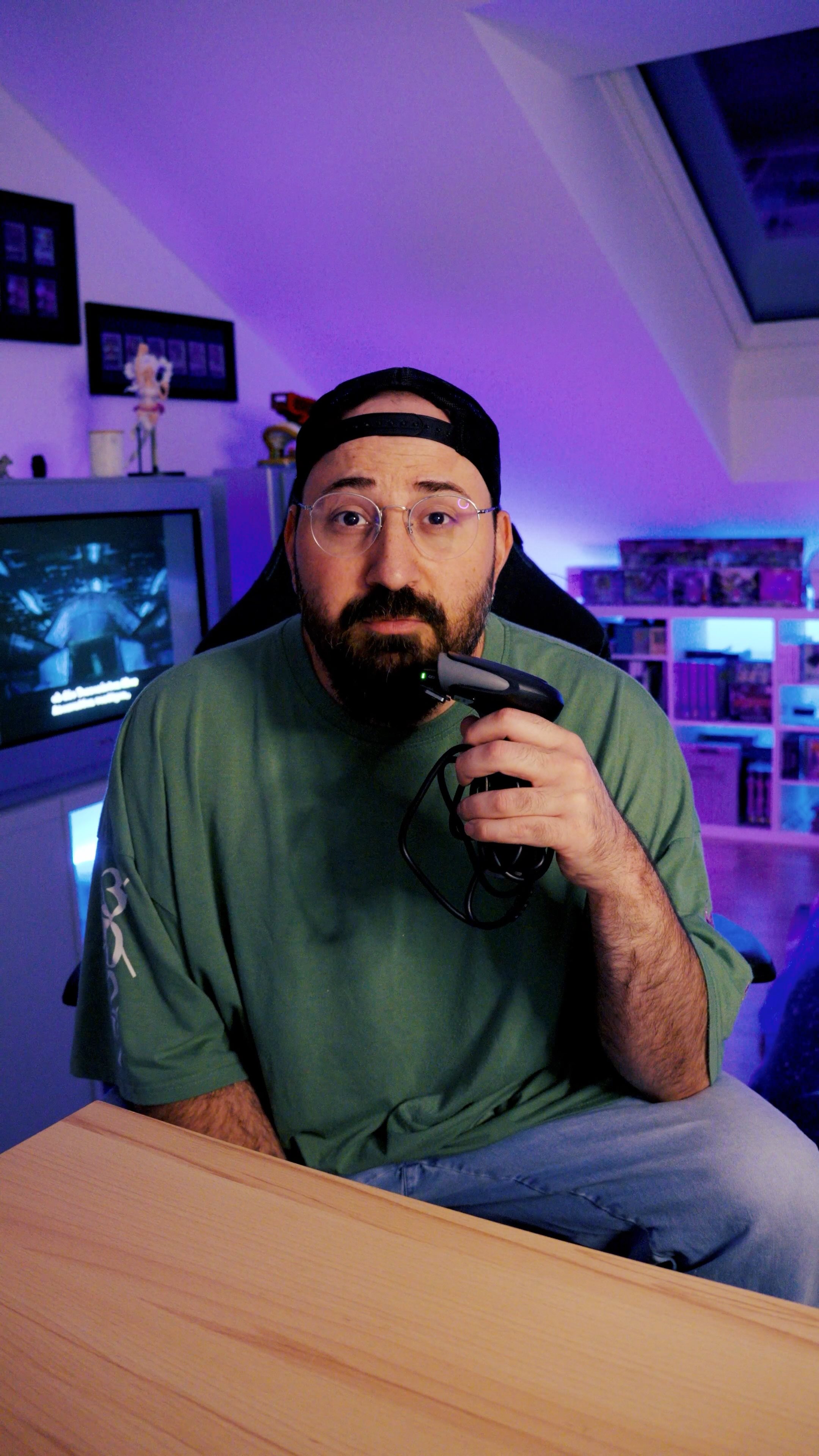 Buri in a green t-shirt holding a game controller in his purple-lit room